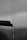 A close-up of a dark, textured pipe with a curved end from which a stream of water is dripping downwards. The background is out of focus, appearing as various shades of gray, giving a soft, blurred effect.