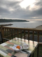 A serene morning scene with breakfast served on a wooden deck by the shore.