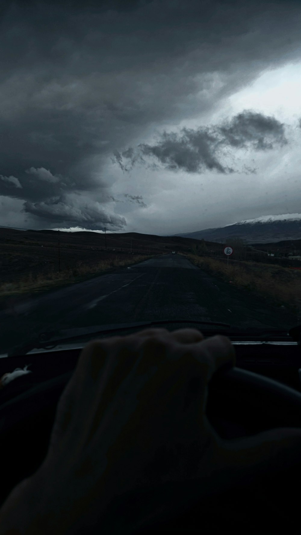 a person driving a car on a road under a cloudy sky