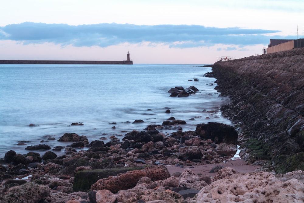 a rocky shore with a lighthouse in the distance