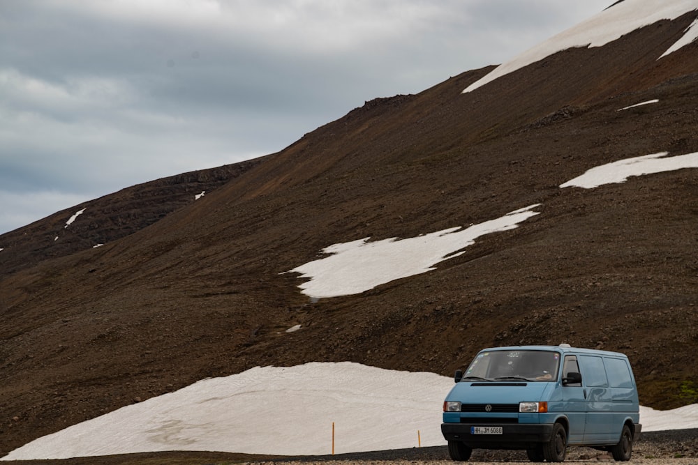 Uma van azul está estacionada em frente a uma montanha