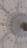 The image features an intricately designed geometric pattern on a wall, resembling a mandala with delicate, pointed shapes radiating from a central point. The color palette includes soft blues and greys, and there is a small, ornate object with gold detailing attached to the wall.
