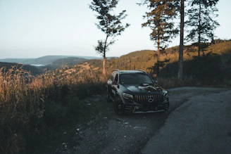 A sleek black SUV parked on a scenic hill station road with sunrise in the background.