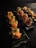 Two black plates are arranged on a dark surface. Each plate holds neatly arranged pieces of sushi rolls garnished with green onions and a creamy sauce. The sushi rolls appear to be wrapped in smoked salmon and a cured meat, possibly prosciutto.