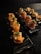 Two black plates are arranged on a dark surface. Each plate holds neatly arranged pieces of sushi rolls garnished with green onions and a creamy sauce. The sushi rolls appear to be wrapped in smoked salmon and a cured meat, possibly prosciutto.