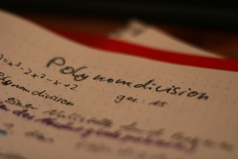 A close-up of handwritten notes on mathematical polynomial division, with a visible equation and the words 'polynomial division' written prominently.