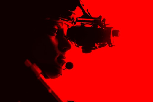 A silhouetted figure is seen side-on against a vibrant red background, wearing night vision goggles. The figure appears to be equipped with a tactical headset, conveying a sense of focus and readiness.