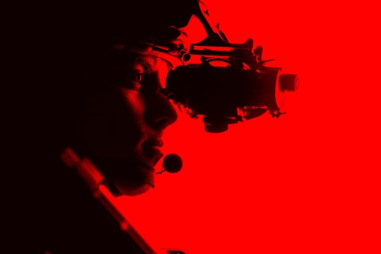 A silhouetted figure is seen side-on against a vibrant red background, wearing night vision goggles. The figure appears to be equipped with a tactical headset, conveying a sense of focus and readiness.