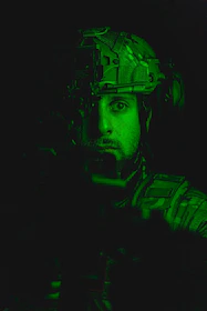 High-definition photo of an elite operator in full tactical gear surveying an industrial perimeter at dusk.