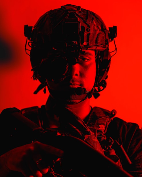 A person wearing tactical gear, including a helmet with attachments and a microphone, is portrayed with a sharp red lighting effect that defines the atmosphere.