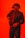 A person wearing a tactical helmet with what appears to be night vision goggles, dressed in a dark suit and tie. The individual is holding a firearm, set against a bright red background, giving the scene a dramatic and intense feel.