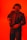 A person wearing a tactical helmet with what appears to be night vision goggles, dressed in a dark suit and tie. The individual is holding a firearm, set against a bright red background, giving the scene a dramatic and intense feel.