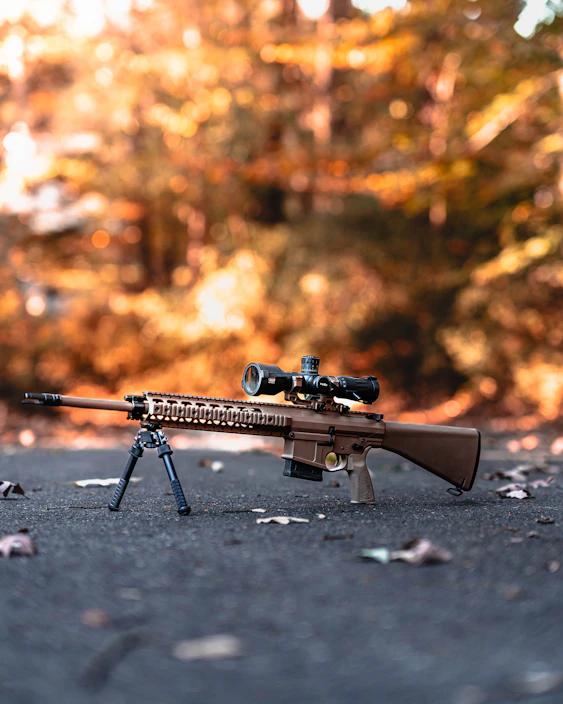 A rugged hunting rifle resting on a wooden table with autumn leaves scattered around.