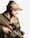 A person wearing camouflage military attire and a beige cap, equipped with over-ear headphones and a microphone. They are holding a tactical rifle with a scope.