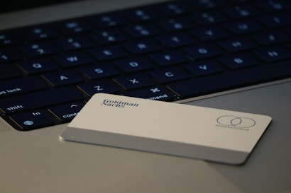 A close-up view of a laptop keyboard with a credit card resting on the surface. The credit card is white and features the logos of Goldman Sachs and Mastercard.