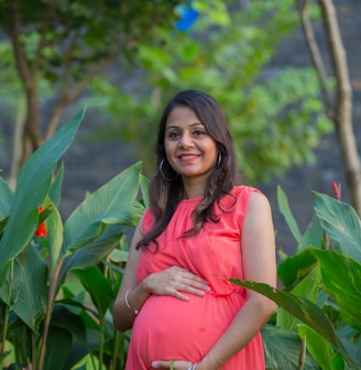 a pregnant woman in a pink dress standing in a garden