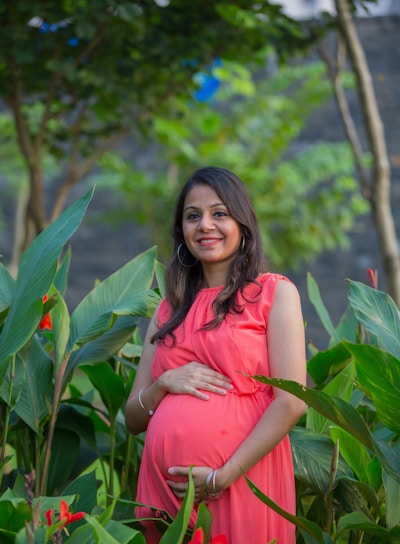 a pregnant woman in a pink dress standing in a garden