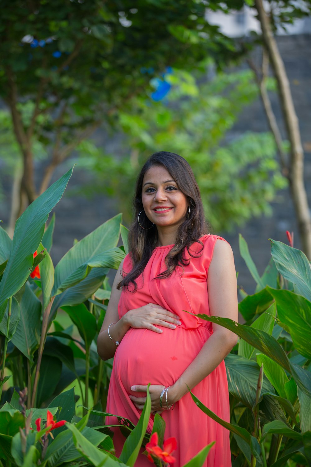 a pregnant woman in a pink dress standing in a garden