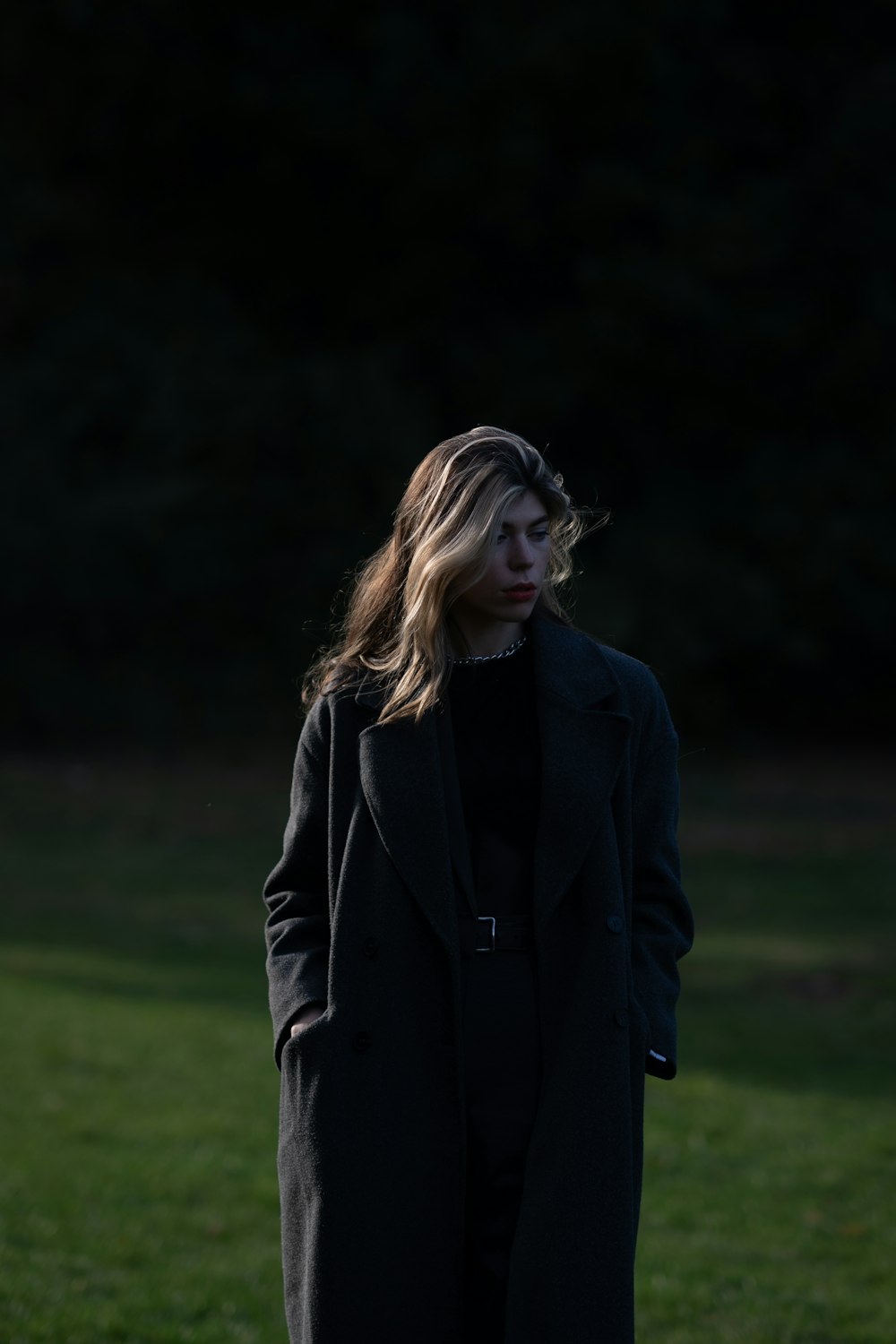 a woman in a black coat standing in a field