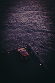 A minimalist sedan parked beside a rustic wooden pier at sunset.