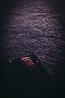 A minimalist sedan parked beside a rustic wooden pier at sunset.
