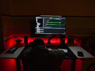 A focused developer working late at a dark-themed desk illuminated by neon blue and green lights.