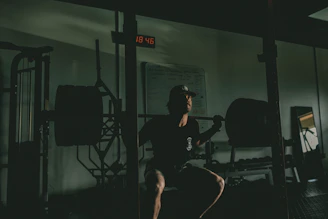 A focused athlete performing a deep squat in a modern gym with dark tones and yellow accents.