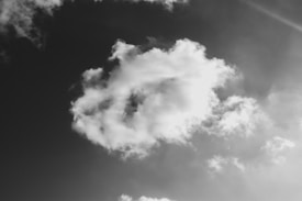 A black-and-white photograph of fluffy clouds floating across a sky. The clouds have a variety of shapes and appear soft and airy, creating a sense of lightness against a darkened sky.