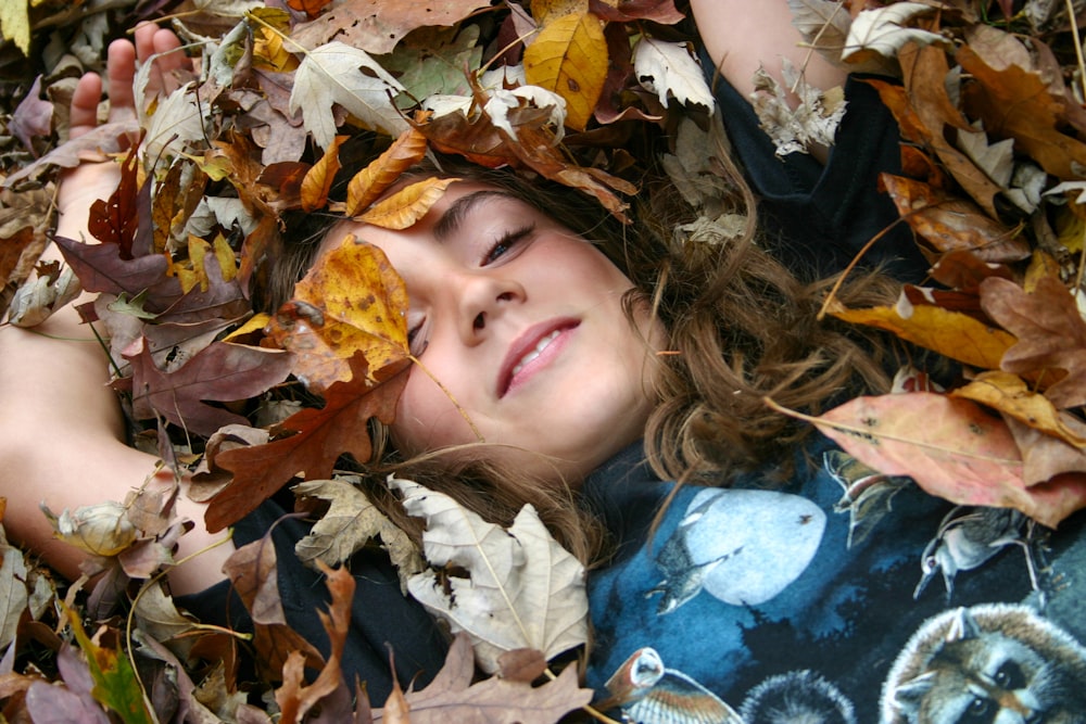 A young girl laying in a pile of leaves photo – Free Leaf Image on