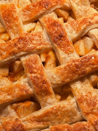 A close-up view of a golden-brown lattice pie crust, showing the flaky texture and baked apples beneath.