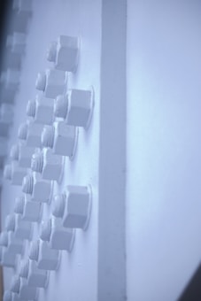 Several hexagonal bolts are arranged in a grid pattern on a light blue surface. The bolts are monochrome and blend seamlessly with the background, creating a minimalist and industrial look.
