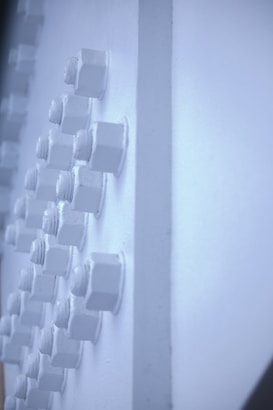 Several hexagonal bolts are arranged in a grid pattern on a light blue surface. The bolts are monochrome and blend seamlessly with the background, creating a minimalist and industrial look.