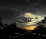 Wide shot of a newly paved highway cutting through rugged terrain at sunset.