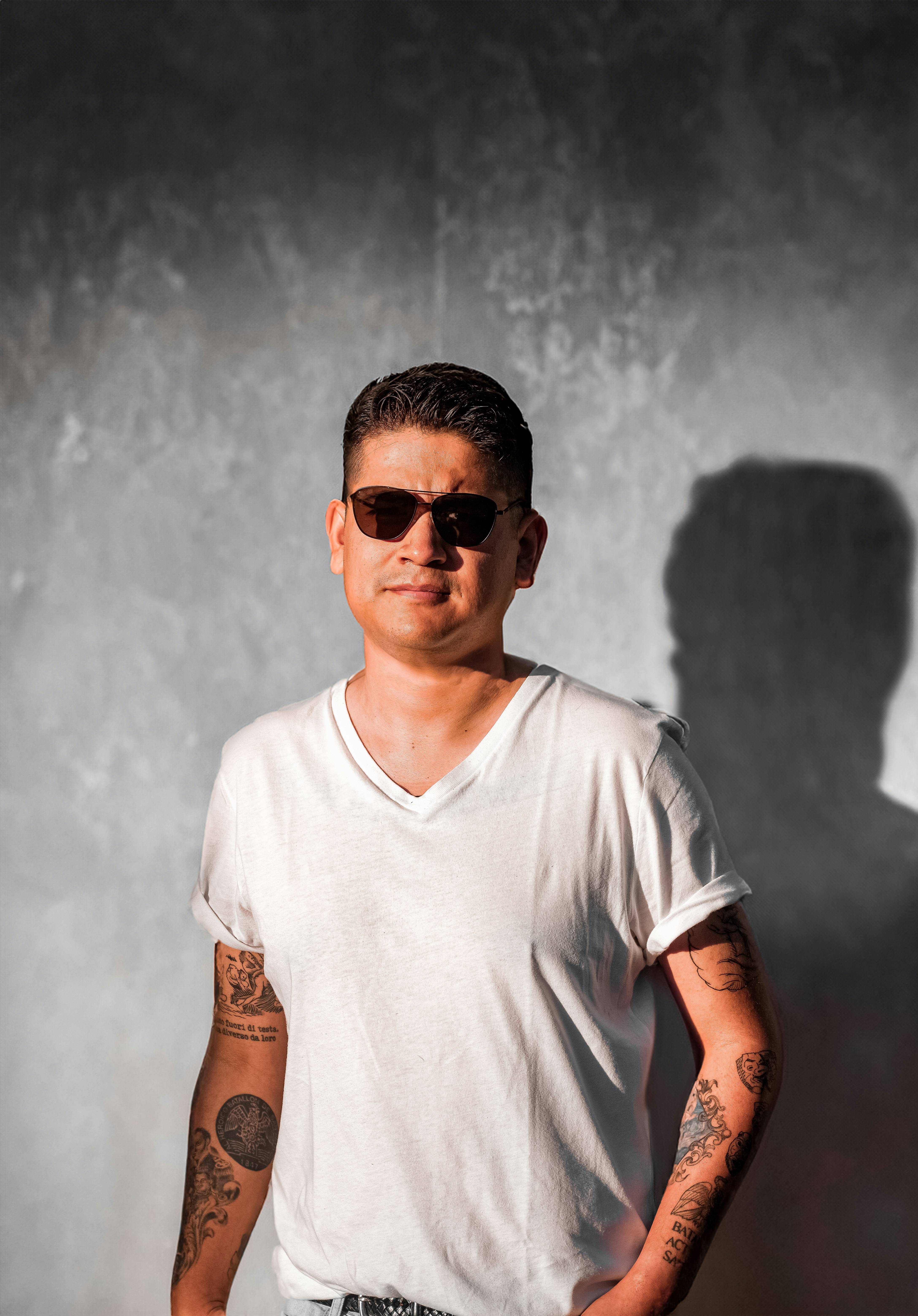 A man in a white shirt and sunglasses standing in front of a wall photo ...