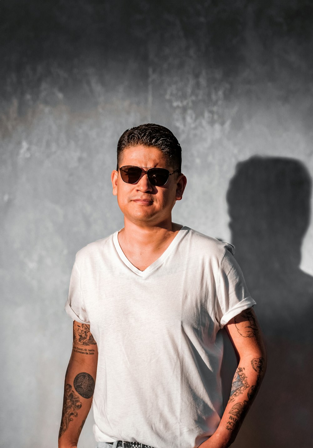 a man in a white shirt and sunglasses standing in front of a wall
