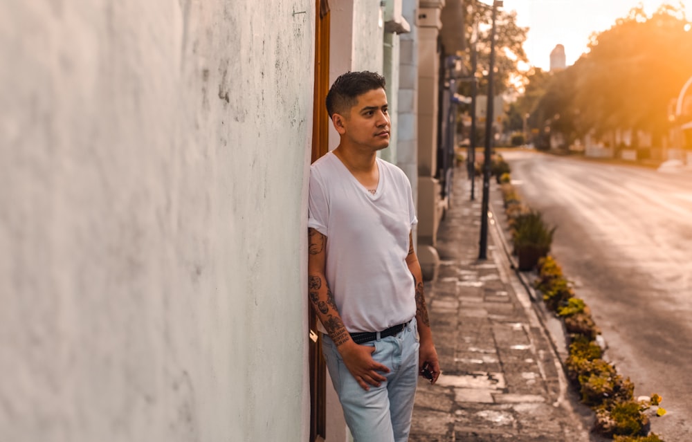 a man leaning against a wall on the side of a street