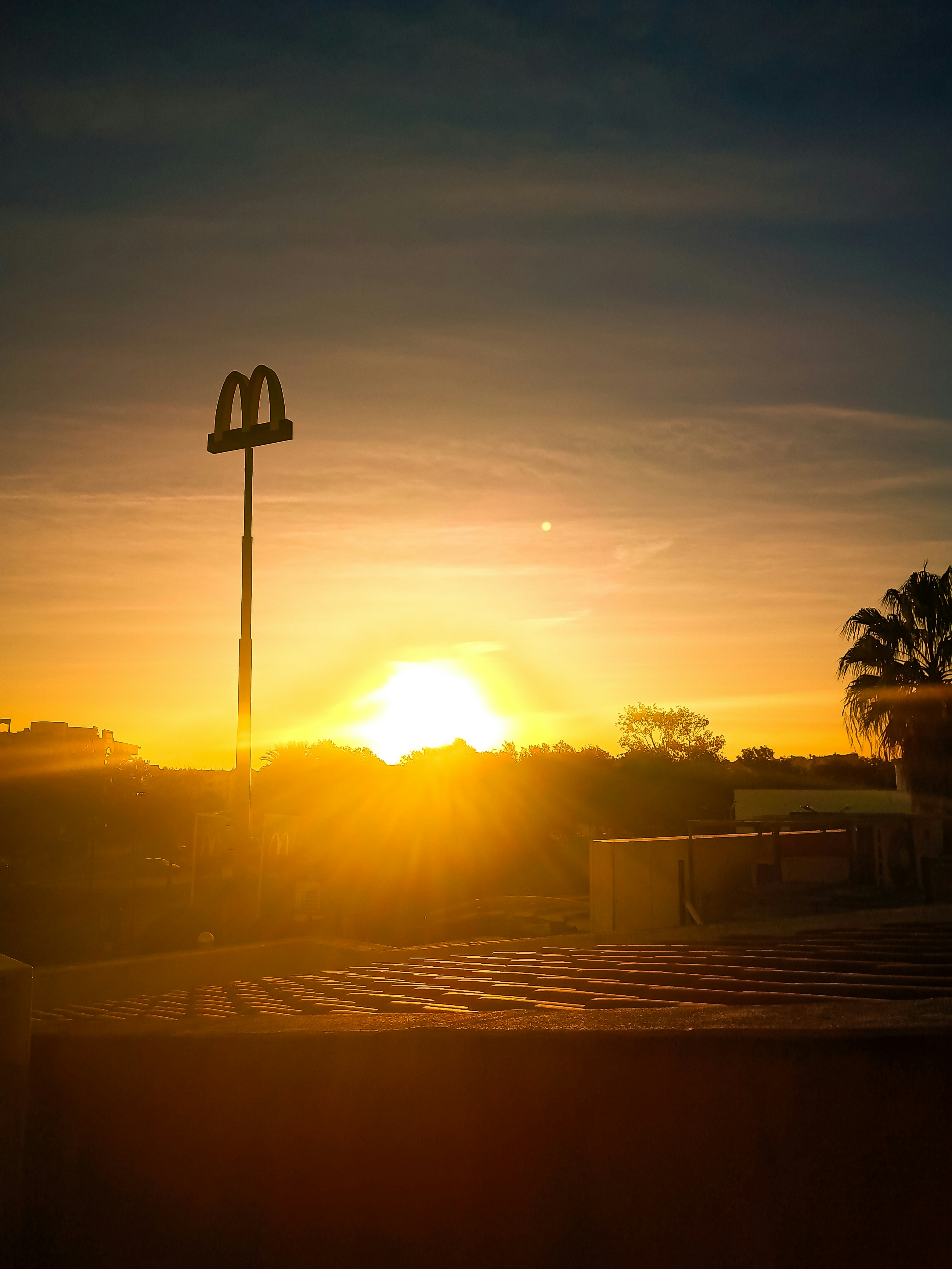 The sun is setting behind a tall light pole photo – Free Outdoors Image