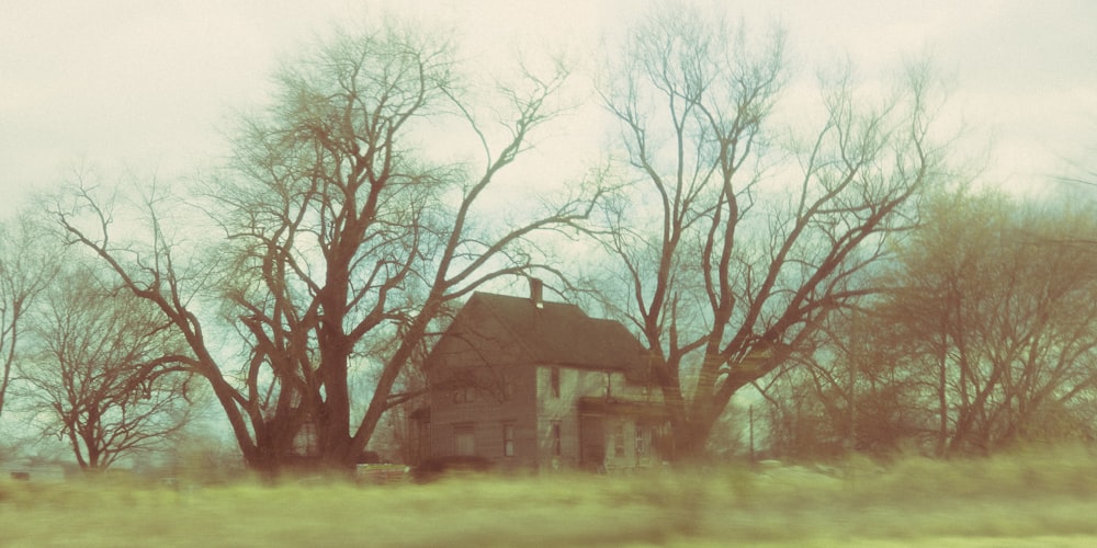 a house in the middle of a field with trees in the background