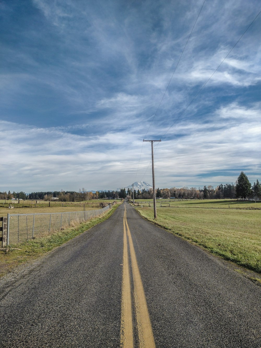 an empty road with a fence and a field in the background