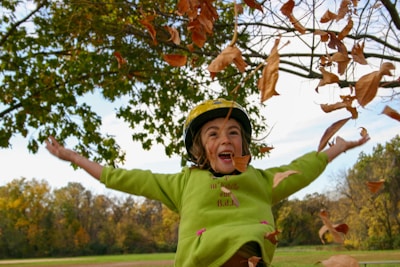 A joyful child wearing an oversized denim jacket and soft hoodie, playing in a sunlit Canadian autumn park with colorful leaves around.
