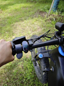 Close-up of a rider's hand gripping the handlebar of a modern e-bike on a forest path.