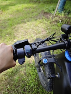 Close-up of a hand gripping the handlebar of a modern electric bike with a digital display.