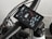 A close-up view of a bicycle handlebar featuring an electronic display with technical readouts. The screen shows information such as speed, distance, and battery percentage. The handlebar and the attached cables are prominently visible, conveying a modern and technical aesthetic.