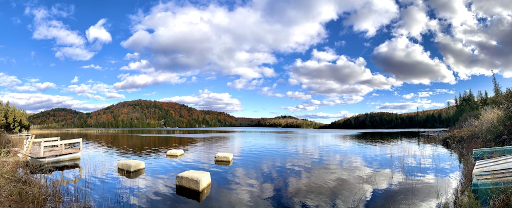 a lake surrounded by mountains and trees under a cloudy blue sky