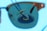 A sunglass lens frames the view of a pool cleaning device submerged in water, creating a contrasting focus against the bright blue of the pool. The lens slightly darkens the view, emphasizing the details of the cleaning equipment with its brush and hose.
