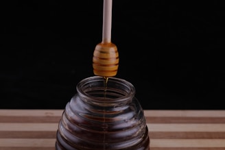 Close-up of golden honey dripping from a wooden honey dipper over a glass jar