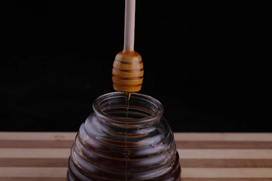 Close-up of golden honey dripping slowly from a wooden honey dipper over a rustic jar.
