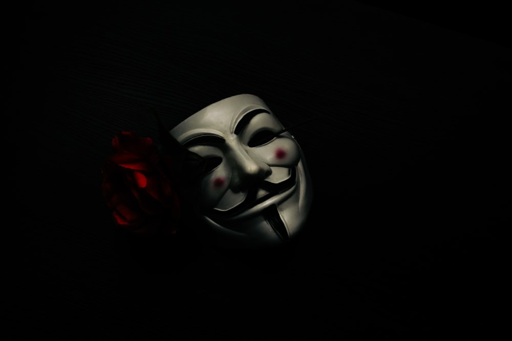 una maschera bianca e una rosa rossa su sfondo nero