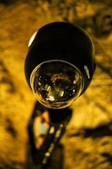 A close-up view of a modern security camera mounted on a wall, with reflections visible on the lens. The background appears to be a textured, warm-colored surface, adding an industrial or rugged aesthetic.