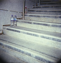 A set of concrete steps with a pair of bottled water on one step and a bottle of aloe drink on a higher step. The steps are lined with metal railings.